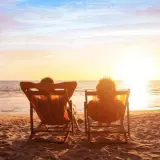 Deux personnes se font dorer la pilule sur des chaises longues, face à un magnifique coucher de soleil sur la mer.