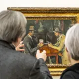 Deux personnes observent une peinture de Cezanne peintre, représentant deux hommes jouant aux cartes.