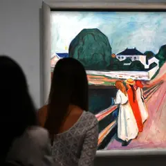 Deux femmes contemplent une œuvre d'Edvard Munch, une scène de rue avec des maisons et des figures colorées.