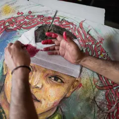 Mains peintes en rouge travaillant sur un portrait, avec des calligraphies arabes rouges vives. Le drapé dans l'art prend une nouvelle dimension.
