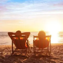 Deux personnes se font dorer la pilule sur des chaises longues, face à un magnifique coucher de soleil sur la mer.