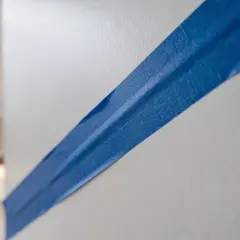 Bande bleue sur mur blanc, créant un contour de lettre stylisé pour un projet de peinture.