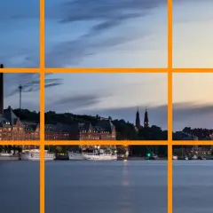 Vue d'un port au crépuscule, avec des bâtiments historiques et des bateaux. La ligne de force de la composition suit le rivage.