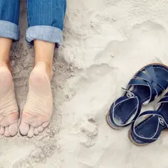 Pieds nus sur le sable, jeans retroussés, et une paire de sandales bleues à côté. On dirait que quelqu'un est prêt à être à côté de ses pompes pour une promenade.
