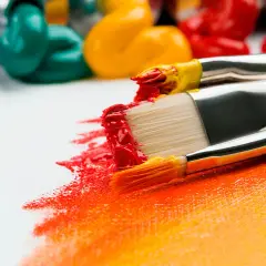 Pinceaux chargés de peinture rouge et jaune, prêts à apprendre la peinture sur une toile blanche. Des tubes de peinture colorée en arrière-plan.