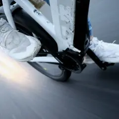 Vue rapprochée des pieds chaussés de baskets blanches pédalant dans la semoule sur un vélo. Le soleil brille à l'horizon.
