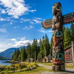 Un voyage dans l'art amérindien : un totem coloré et des maisons sculptées se dressent devant un lac et des montagnes majestueuses.