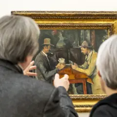 Deux personnes observent une peinture de Cezanne peintre, représentant deux hommes jouant aux cartes.