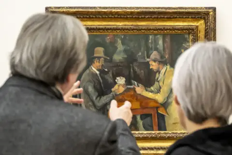 Deux personnes observent une peinture de Cezanne peintre, représentant deux hommes jouant aux cartes.