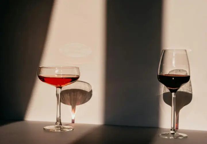 Deux verres de vin, l'un rouge clair, l'autre plus foncé, se dressent dans la lumière. Leurs ombres dansent sur le mur, évoquant l'origine de l'eau.