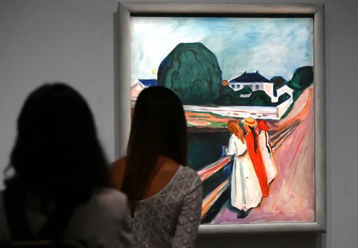 Deux femmes contemplent une œuvre d'Edvard Munch, une scène de rue avec des maisons et des figures colorées.