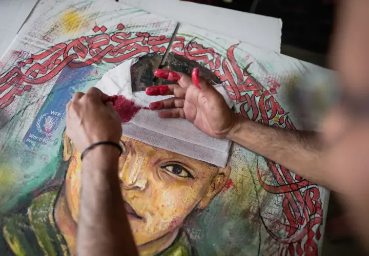 Mains peintes en rouge travaillant sur un portrait, avec des calligraphies arabes rouges vives. Le drapé dans l'art prend une nouvelle dimension.