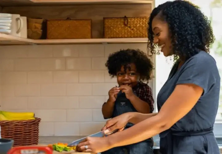 Une mère et son enfant préparent des légumes dans la cuisine. L'enfant grignote, la mère coupe. Tous les goûts sont dans la nature, même pour les plus petits !