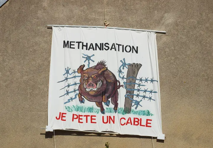 Bannière "METHANISATION" avec un sanglier en colère, prêt à péter un cable, traversant une clôture barbelée.