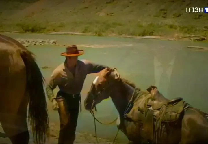 Un cow-boy, prêt à monter sur ses grands chevaux, caresse son compagnon près d'une rivière.