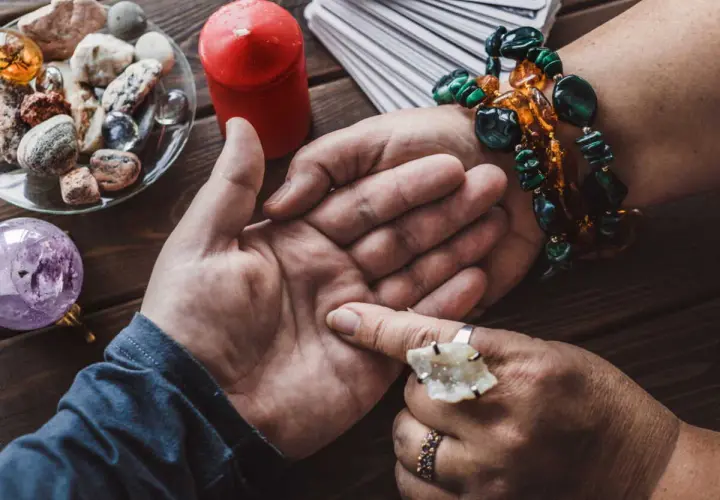 Une voyante lit l'avenir dans la paume d'une main, avec des cartes, une boule de cristal et des pierres. Elle semble avoir la main sur le cœur, concentrée.