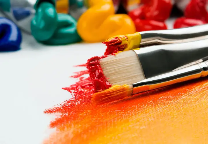 Pinceaux chargés de peinture rouge et jaune, prêts à apprendre la peinture sur une toile blanche. Des tubes de peinture colorée en arrière-plan.
