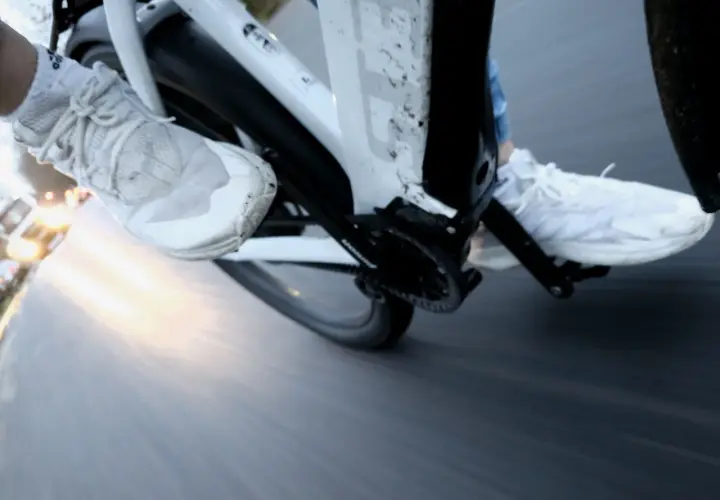 Vue rapprochée des pieds chaussés de baskets blanches pédalant dans la semoule sur un vélo. Le soleil brille à l'horizon.