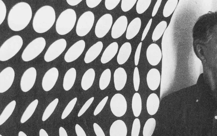 Un homme pose devant une œuvre op art de Vasarely, un motif de cercles blancs sur fond noir créant une illusion de mouvement.
