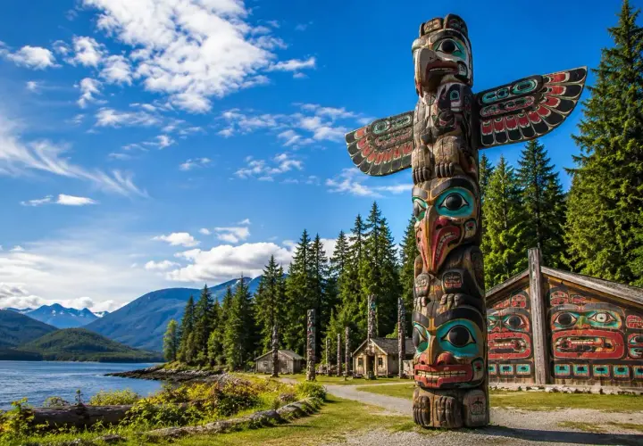 Un voyage dans l'art amérindien : un totem coloré et des maisons sculptées se dressent devant un lac et des montagnes majestueuses.