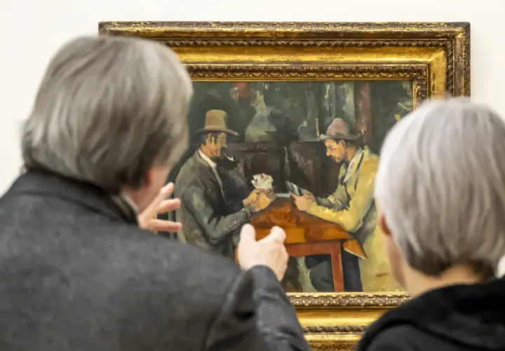 Deux personnes observent une peinture de Cezanne peintre, représentant deux hommes jouant aux cartes.