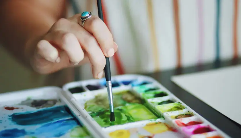 Main d'une artiste avec une bague turquoise, tenant un pinceau au-dessus d'une palette de couleurs vives pour une aquarelle peinture.