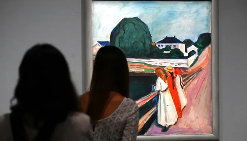 Deux femmes contemplent une œuvre d'Edvard Munch, une scène de rue avec des maisons et des figures colorées.