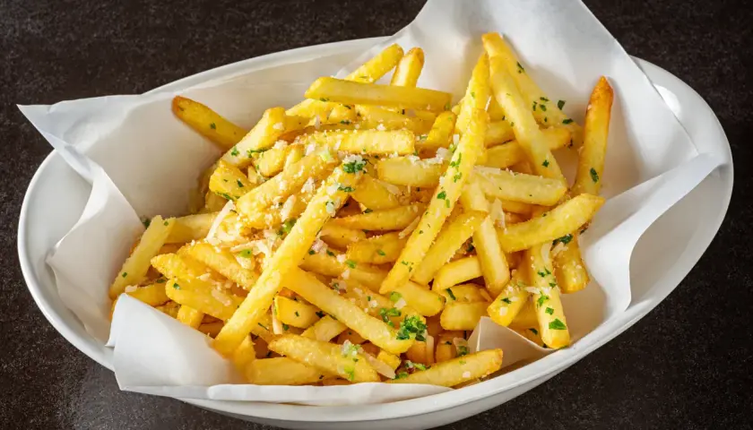 Un plat de frites dorées, parsemées de persil et de parmesan, qui donne envie d'avoir la frite !