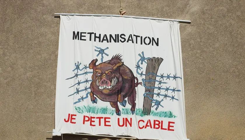 Bannière "METHANISATION" avec un sanglier en colère, prêt à péter un cable, traversant une clôture barbelée.