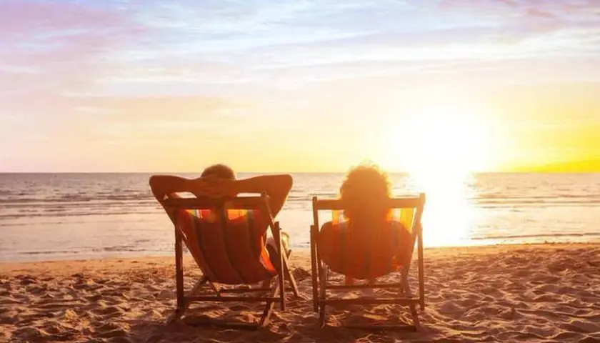 Deux personnes se font dorer la pilule sur des chaises longues, face à un magnifique coucher de soleil sur la mer.