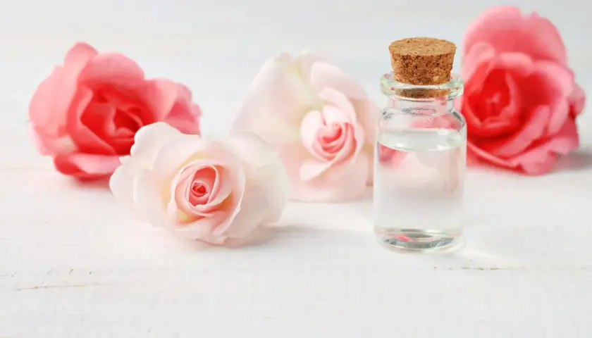Un flacon de verre bouché de liège contient un liquide clair, entouré de roses roses et pâles. L'expression de l'eau de rose évoque la douceur et la pureté.