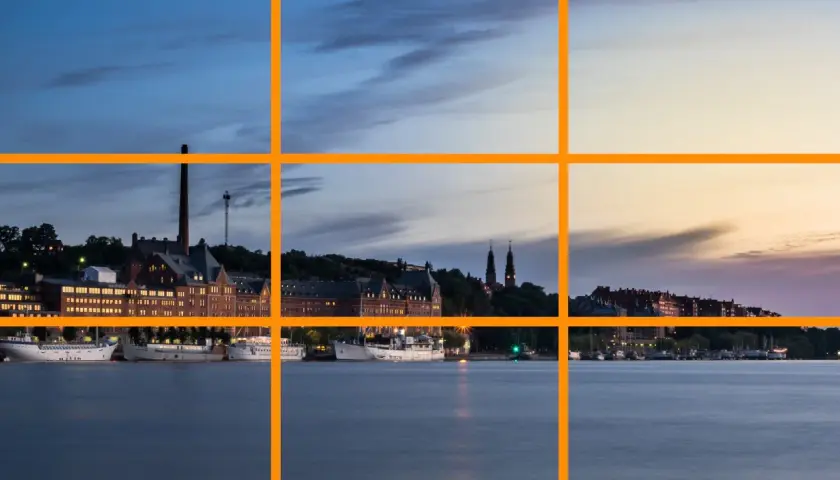 Vue d'un port au crépuscule, avec des bâtiments historiques et des bateaux. La ligne de force de la composition suit le rivage.