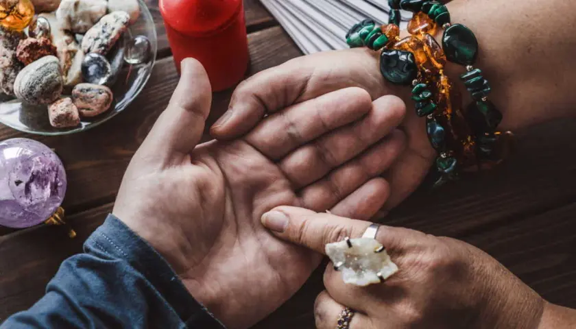 Une voyante lit l'avenir dans la paume d'une main, avec des cartes, une boule de cristal et des pierres. Elle semble avoir la main sur le cœur, concentrée.