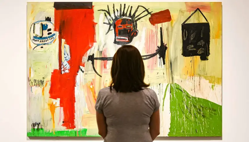 Une femme admire une peinture vibrante dans un style Basquiat, avec un visage expressif au centre et des formes abstraites.