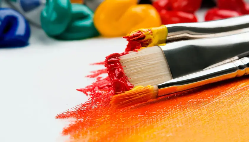 Pinceaux chargés de peinture rouge et jaune, prêts à apprendre la peinture sur une toile blanche. Des tubes de peinture colorée en arrière-plan.