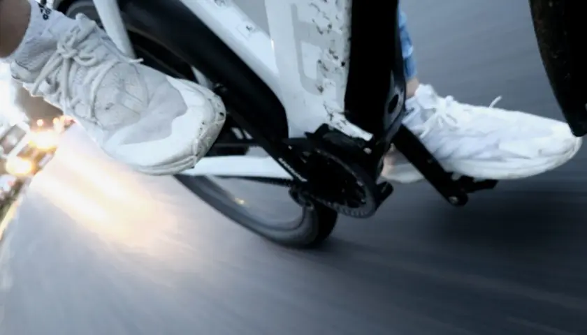 Vue rapprochée des pieds chaussés de baskets blanches pédalant dans la semoule sur un vélo. Le soleil brille à l'horizon.