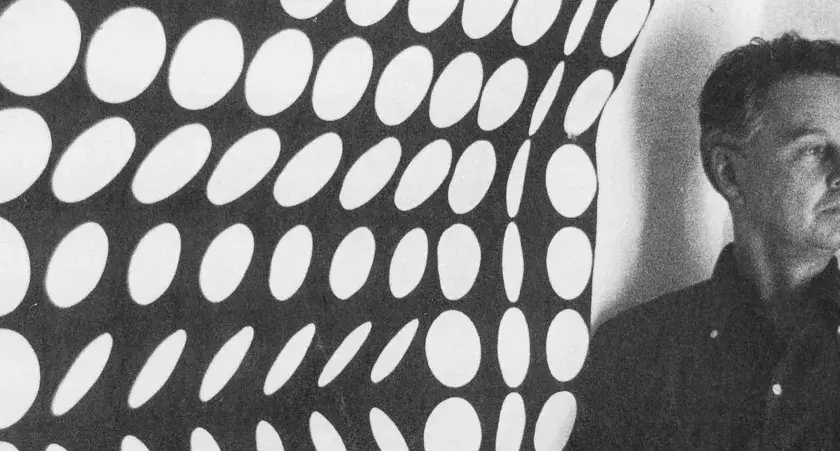 Un homme pose devant une œuvre op art de Vasarely, un motif de cercles blancs sur fond noir créant une illusion de mouvement.