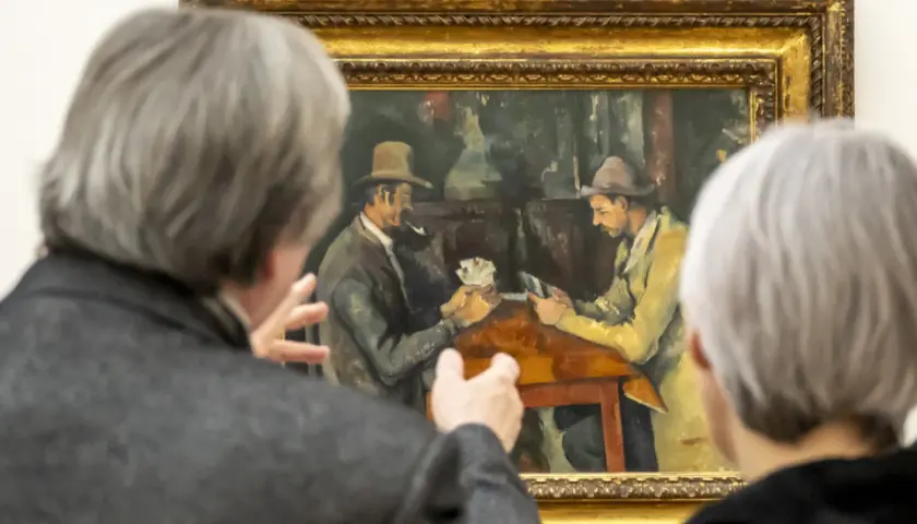 Deux personnes observent une peinture de Cezanne peintre, représentant deux hommes jouant aux cartes.