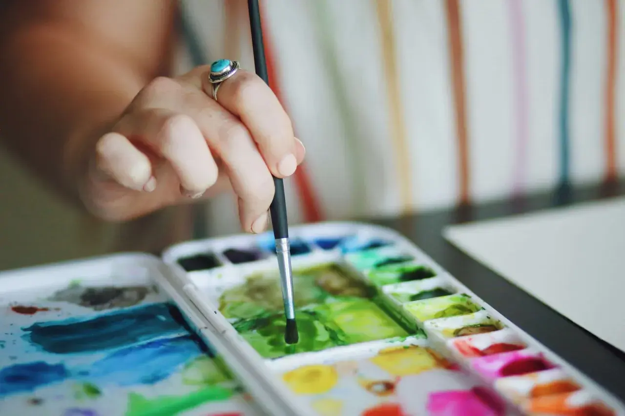 Main d'une artiste avec une bague turquoise, tenant un pinceau au-dessus d'une palette de couleurs vives pour une aquarelle peinture.