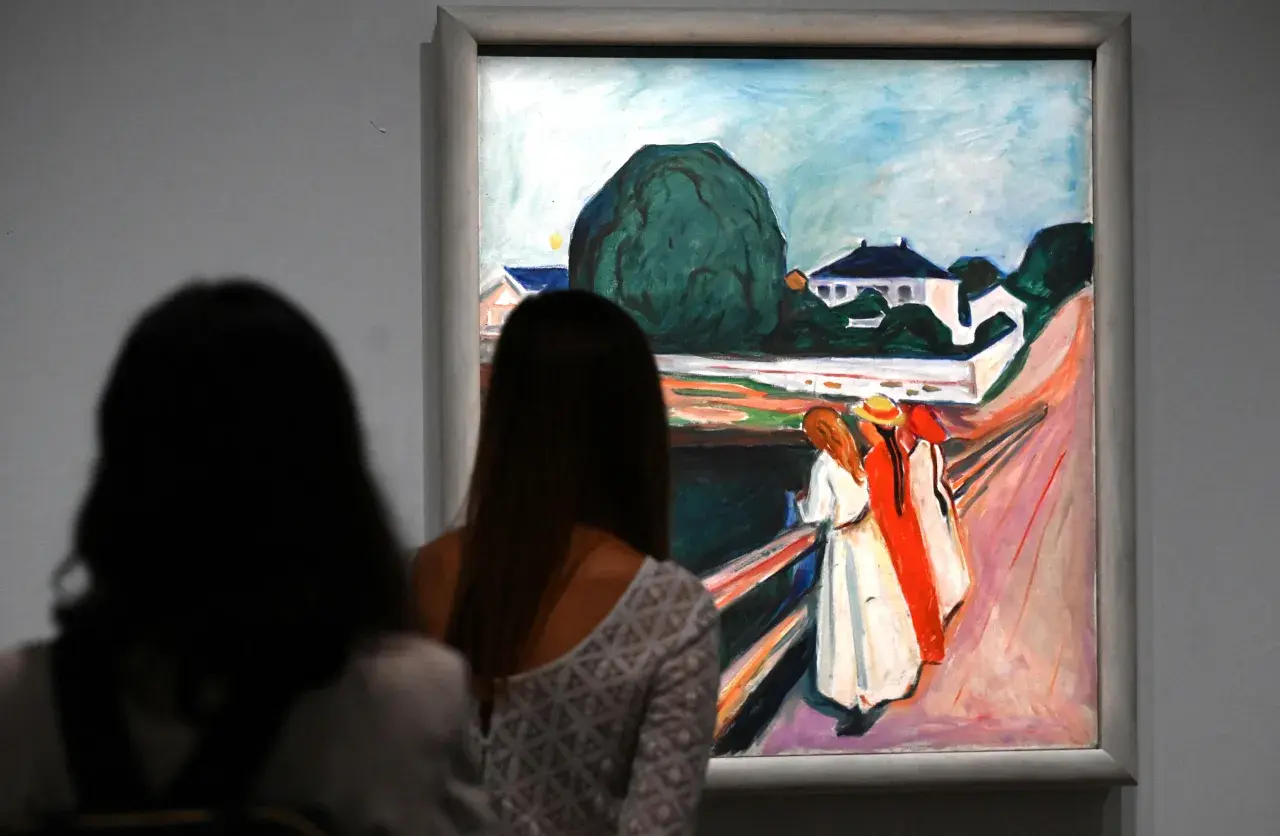 Deux femmes contemplent une œuvre d'Edvard Munch, une scène de rue avec des maisons et des figures colorées.