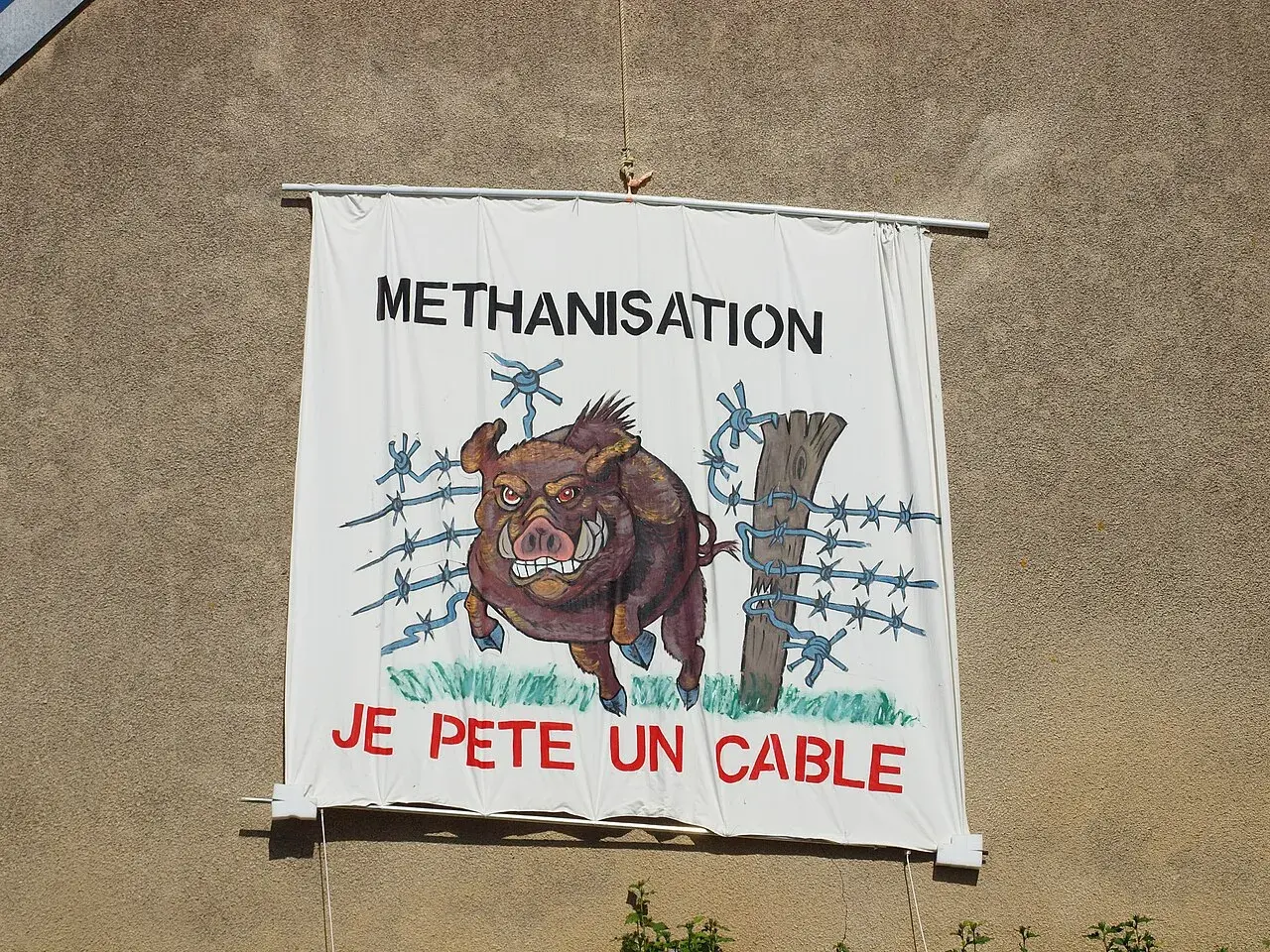 Bannière "METHANISATION" avec un sanglier en colère, prêt à péter un cable, traversant une clôture barbelée.