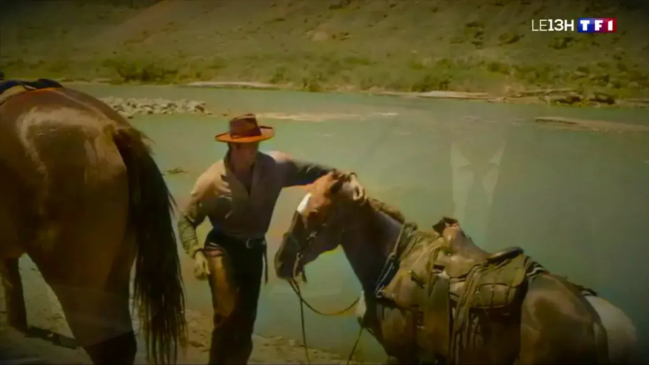 Un cow-boy, prêt à monter sur ses grands chevaux, caresse son compagnon près d'une rivière.