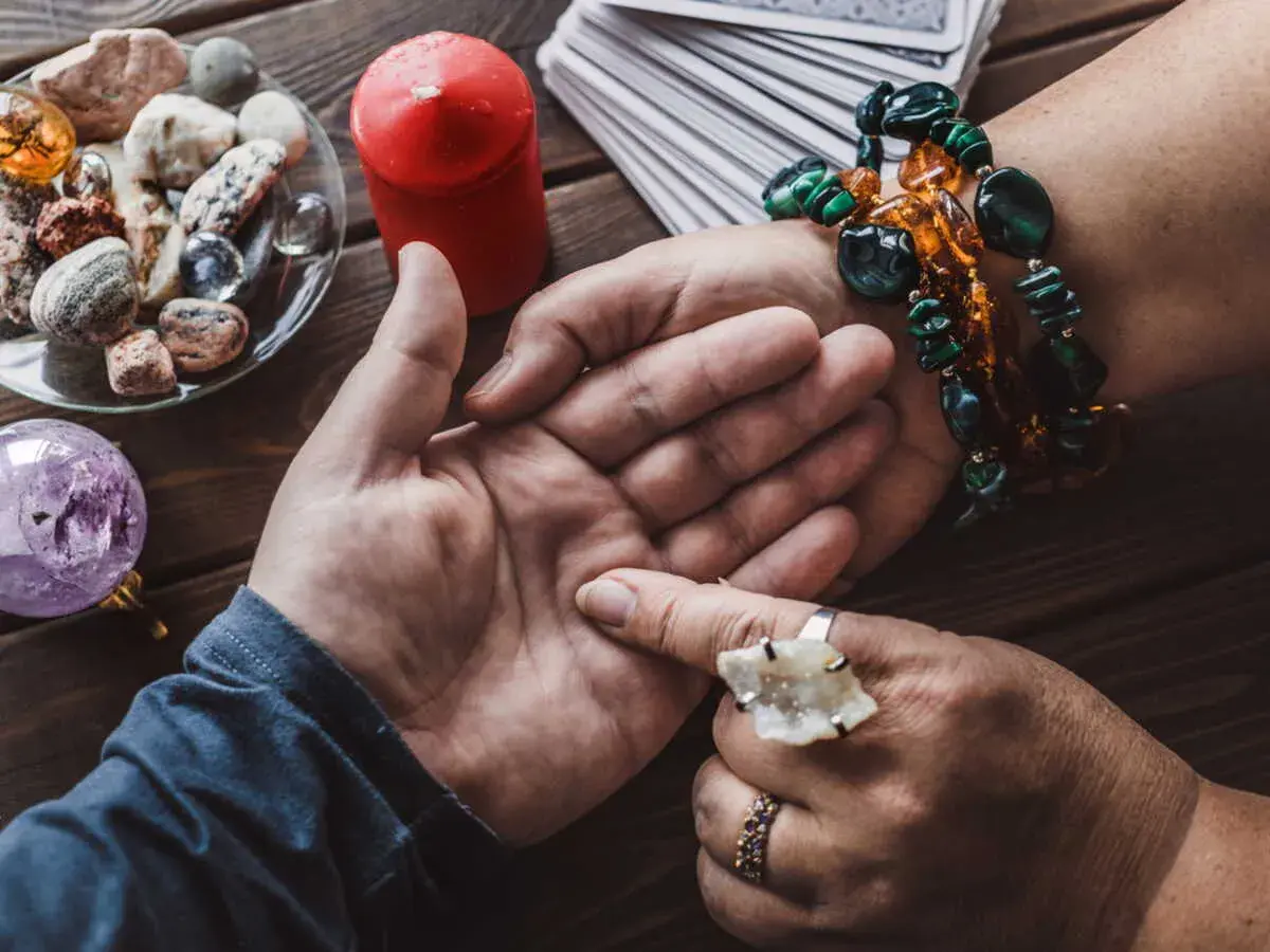 Une voyante lit l'avenir dans la paume d'une main, avec des cartes, une boule de cristal et des pierres. Elle semble avoir la main sur le cœur, concentrée.