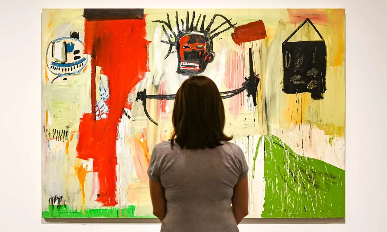 Une femme admire une peinture vibrante dans un style Basquiat, avec un visage expressif au centre et des formes abstraites.