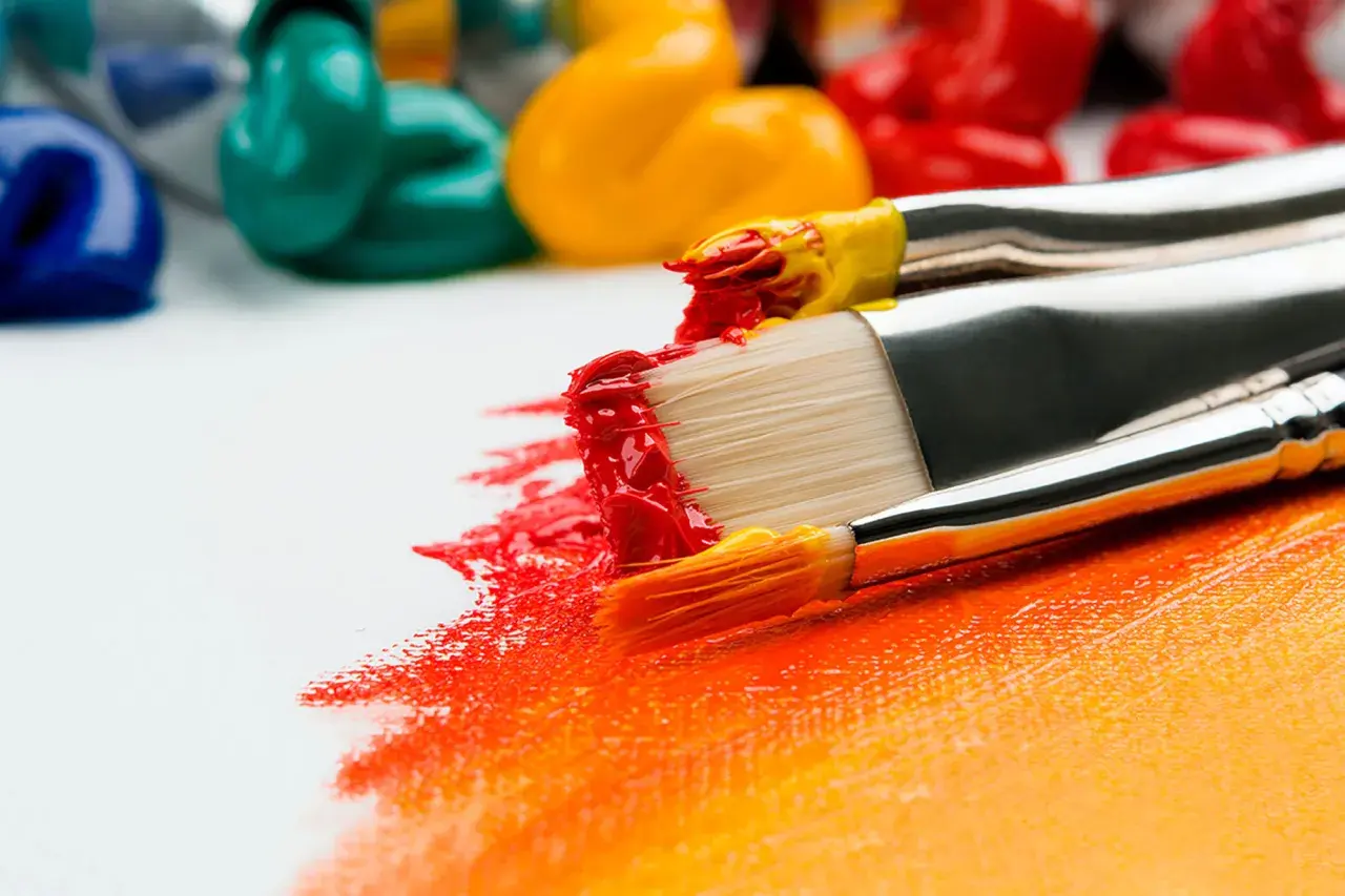 Pinceaux chargés de peinture rouge et jaune, prêts à apprendre la peinture sur une toile blanche. Des tubes de peinture colorée en arrière-plan.