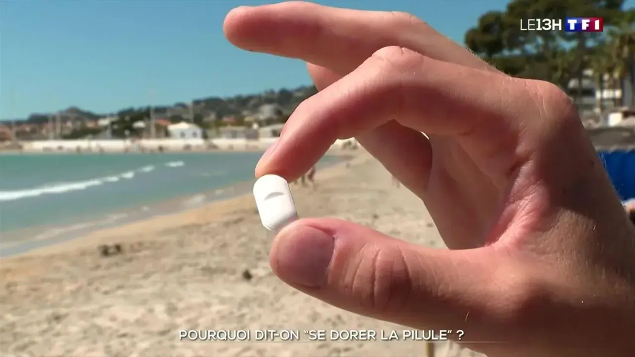 Main d'un homme tenant une pilule blanche sur une plage ensoleillée, interrogeant sur l'expression "se dorer la pilule".