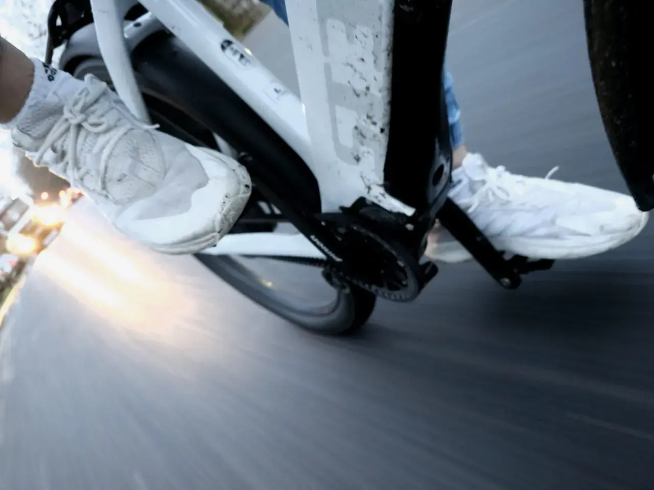 Vue rapprochée des pieds chaussés de baskets blanches pédalant dans la semoule sur un vélo. Le soleil brille à l'horizon.