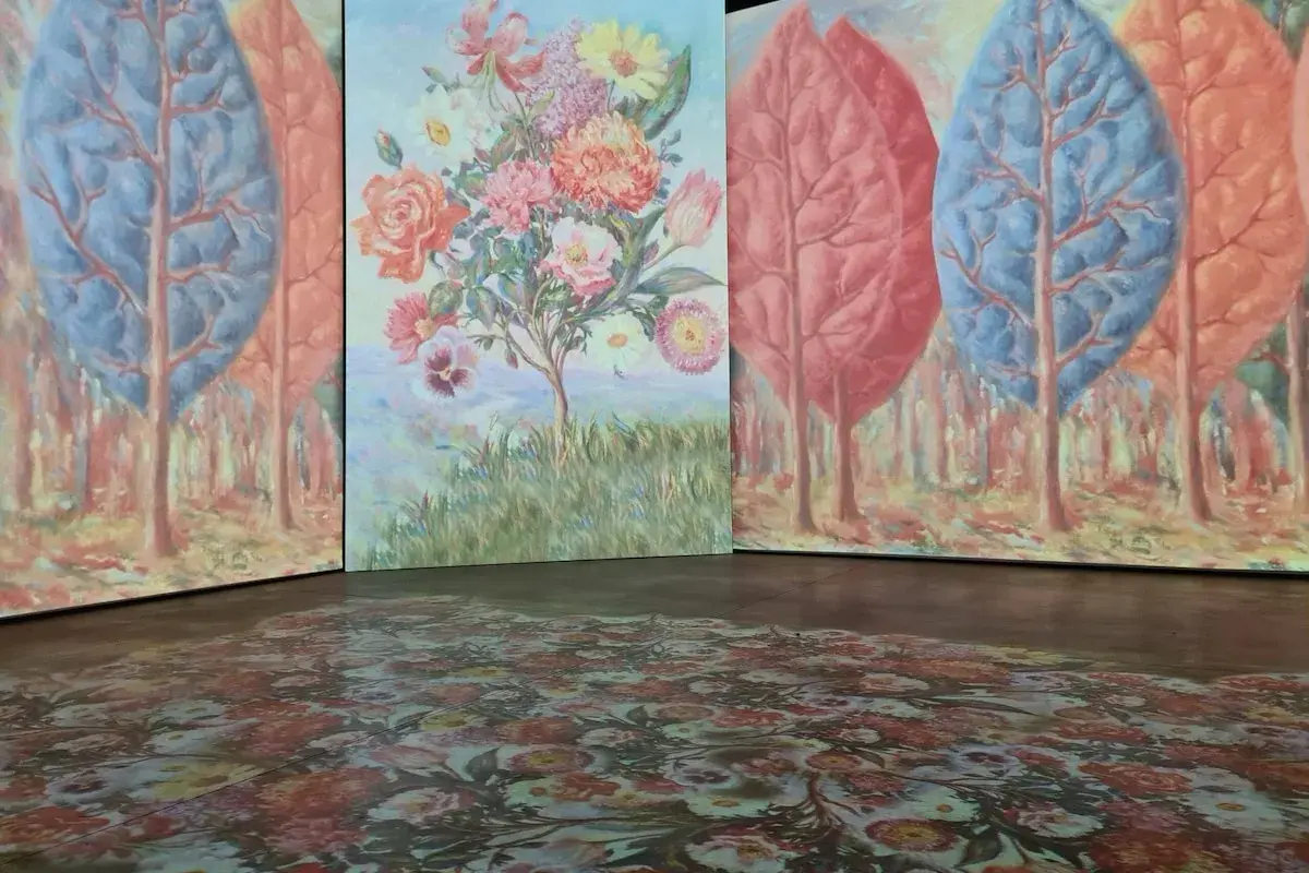 Installation d'art avec des arbres stylisés et un bouquet de fleurs, évoquant l'univers d'un peintre belge. Le sol est orné d'un motif floral projeté.
