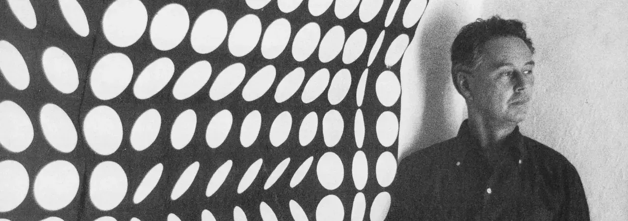 Un homme pose devant une œuvre op art de Vasarely, un motif de cercles blancs sur fond noir créant une illusion de mouvement.