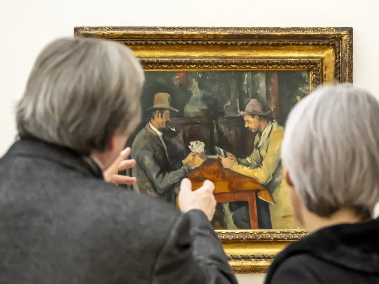 Deux personnes observent une peinture de Cezanne peintre, représentant deux hommes jouant aux cartes.